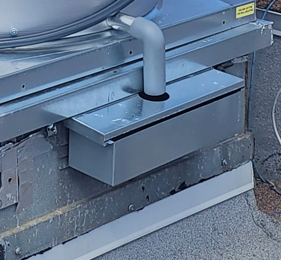 Metal grease catcher beneath the exhaust fan drain pipe, collecting grease above the roof